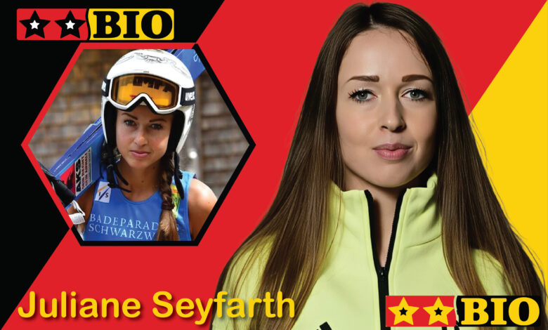 Porträt der deutschen Skispringerin Juliane Seyfarth in professioneller Sportausrüstung mit ihren Sprungskiern vor einer winterlichen Schanzenkulisse